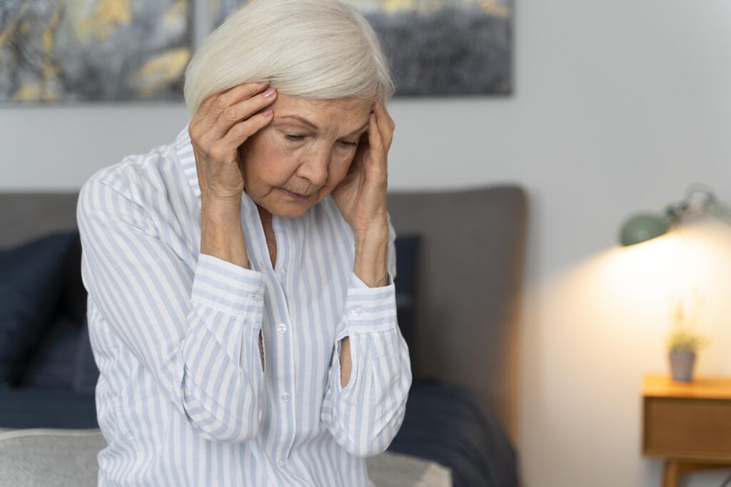 An elderly woman is holding her head in pain.