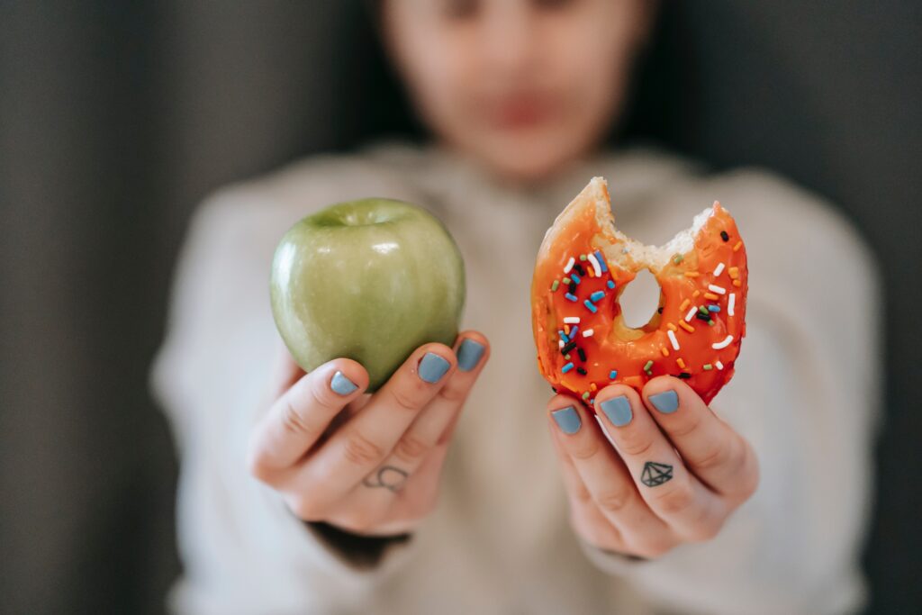 A woman holding an apple and a donut.