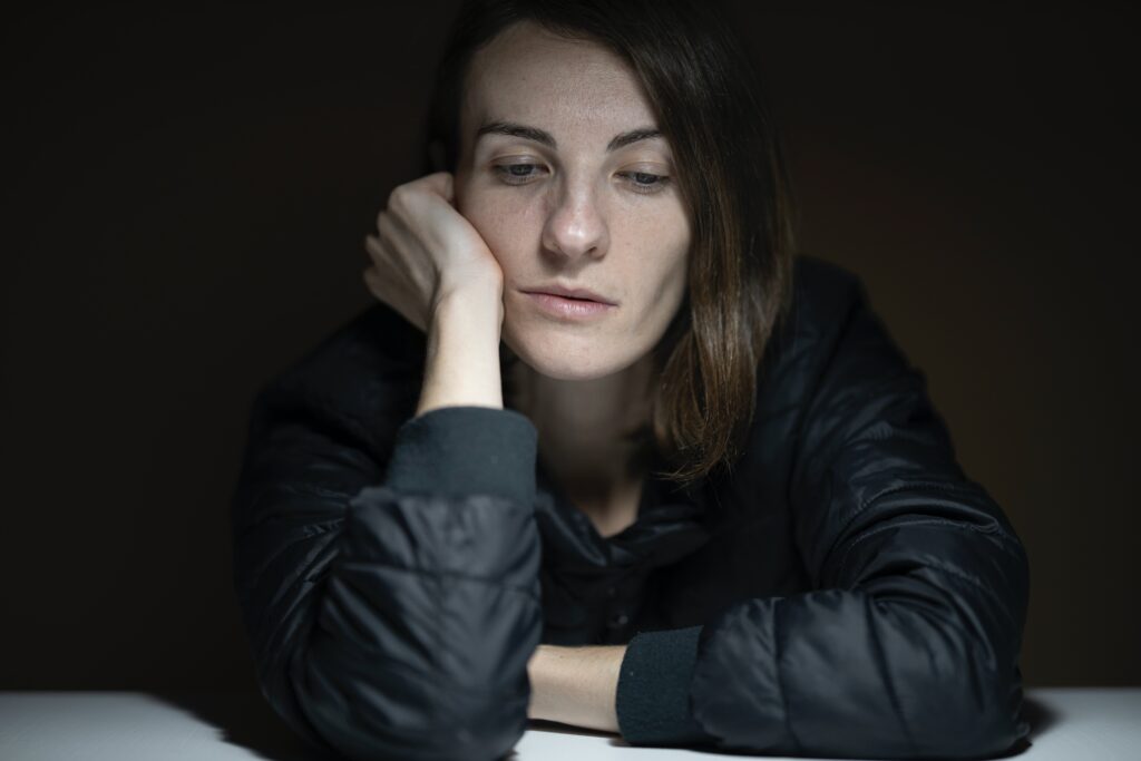 A woman is sitting at a table in the dark, displaying signs of depression.