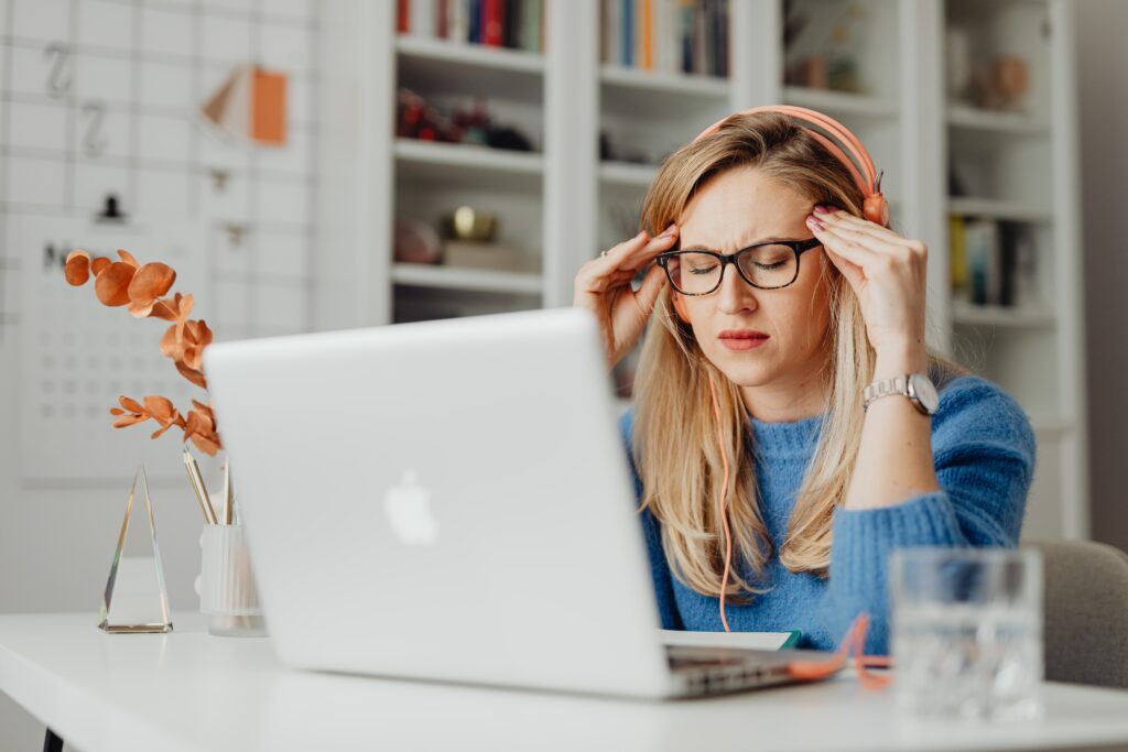 A woman wearing a headache relief cap is sitting at a desk with headphones on her head.