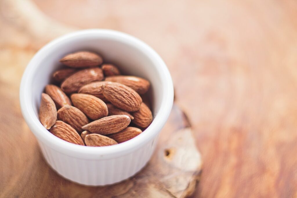 A white bowl filled with whole almonds on a wooden surface.